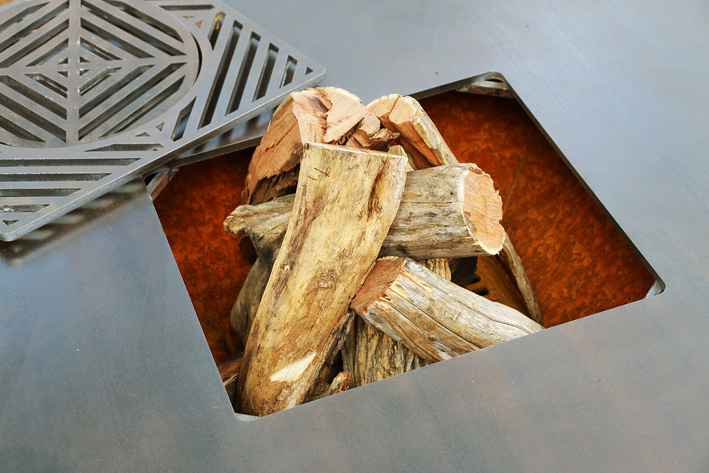 Close view of the Chad-O-Chef Boma Braai firebox loaded with wood, with the cast trivet lifted to one side